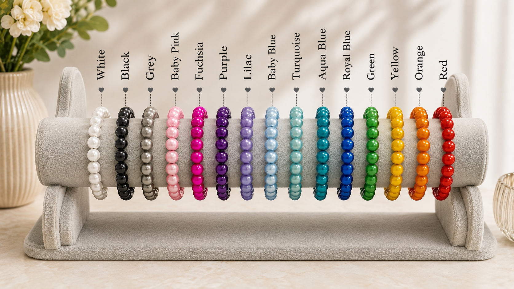 A display stand holding multiple beaded stretch bracelets in different colors, with color labels above each bracelet including White, Black, Grey, Baby Pink, Fuchsia, Purple, Lilac, Baby Blue, Turquoise, Royal Blue, Green, Yellow, Orange, and Red.