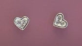Heart-shaped silver earrings with clear stones on a pink background