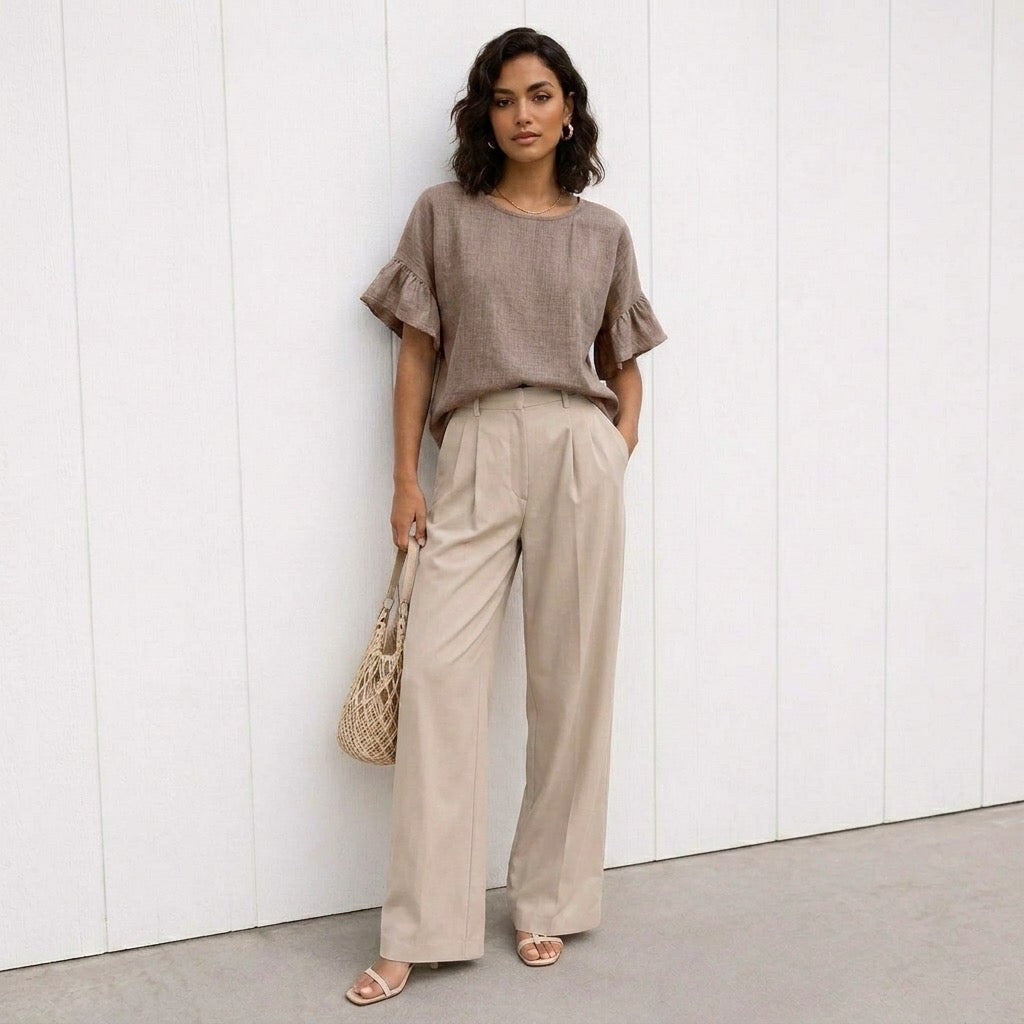Woman wearing a brown top and beige pants against a white wall