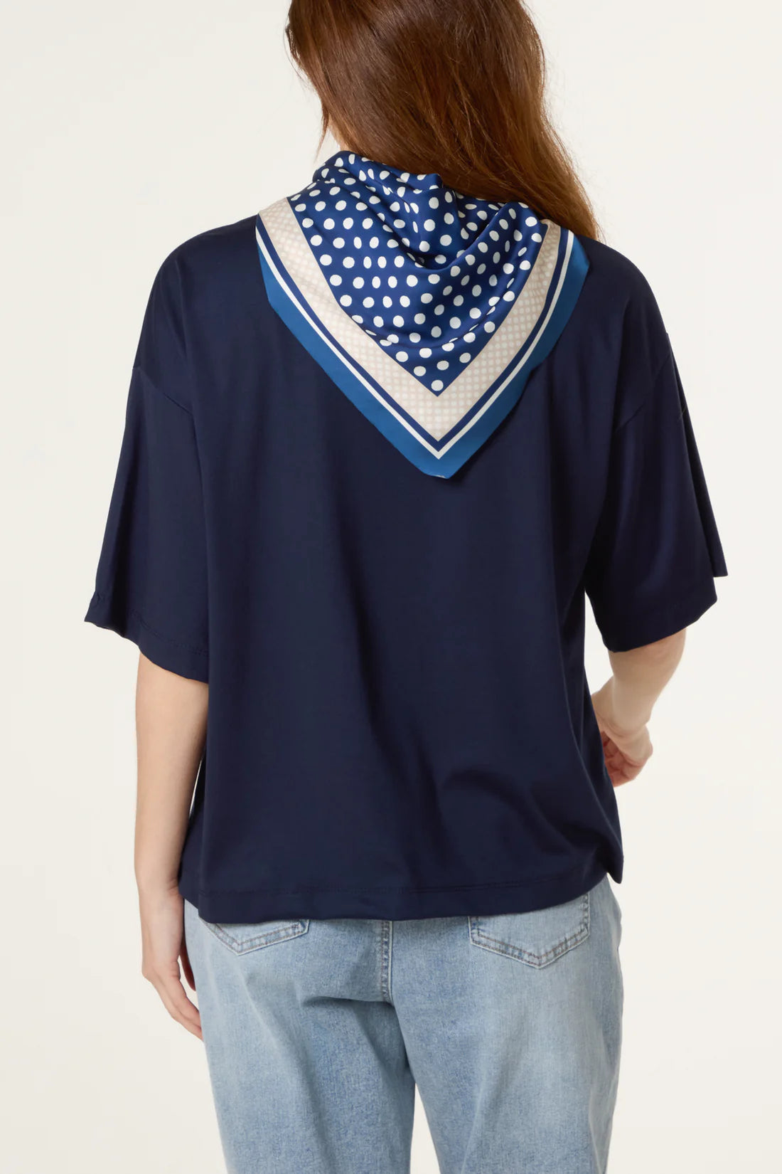 Person wearing a navy blue top with a polka dot scarf on a plain background