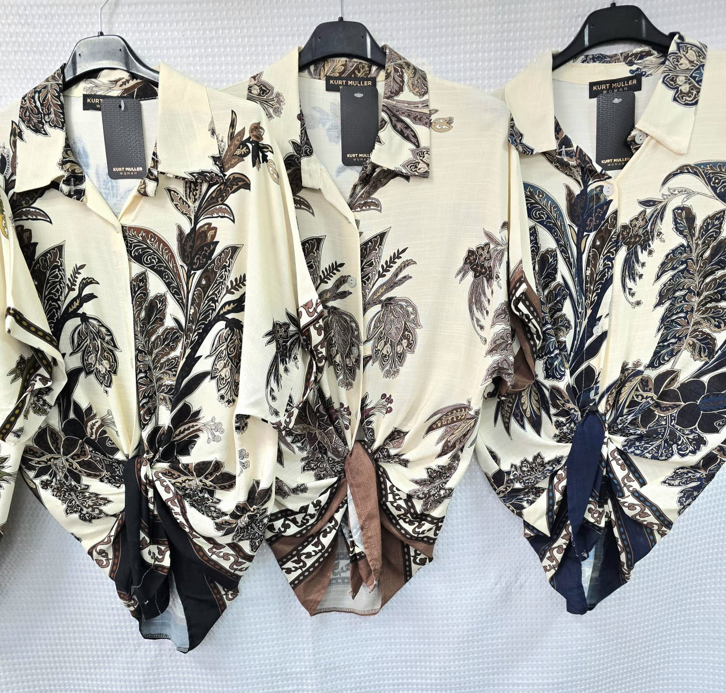 Three floral-patterned shirts on hangers with tags, displayed against a light background.