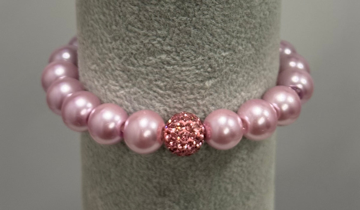 A pink beaded bracelet with a textured, sparkling pink central bead, displayed on a gray fabric jewelry stand.