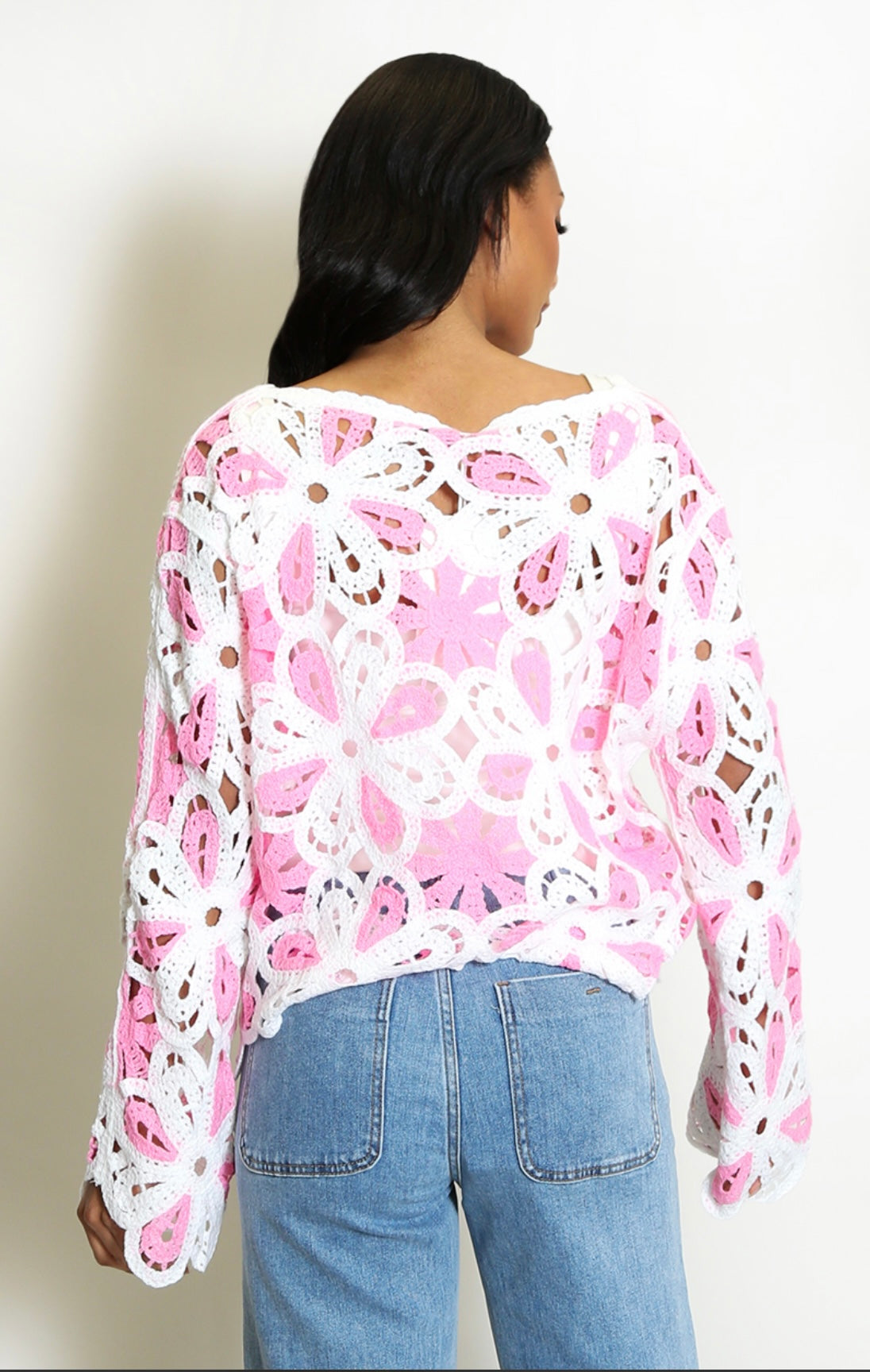 Back View Person wearing a Pink and White Floral Crochet Jumper with blue jeans on a plain background