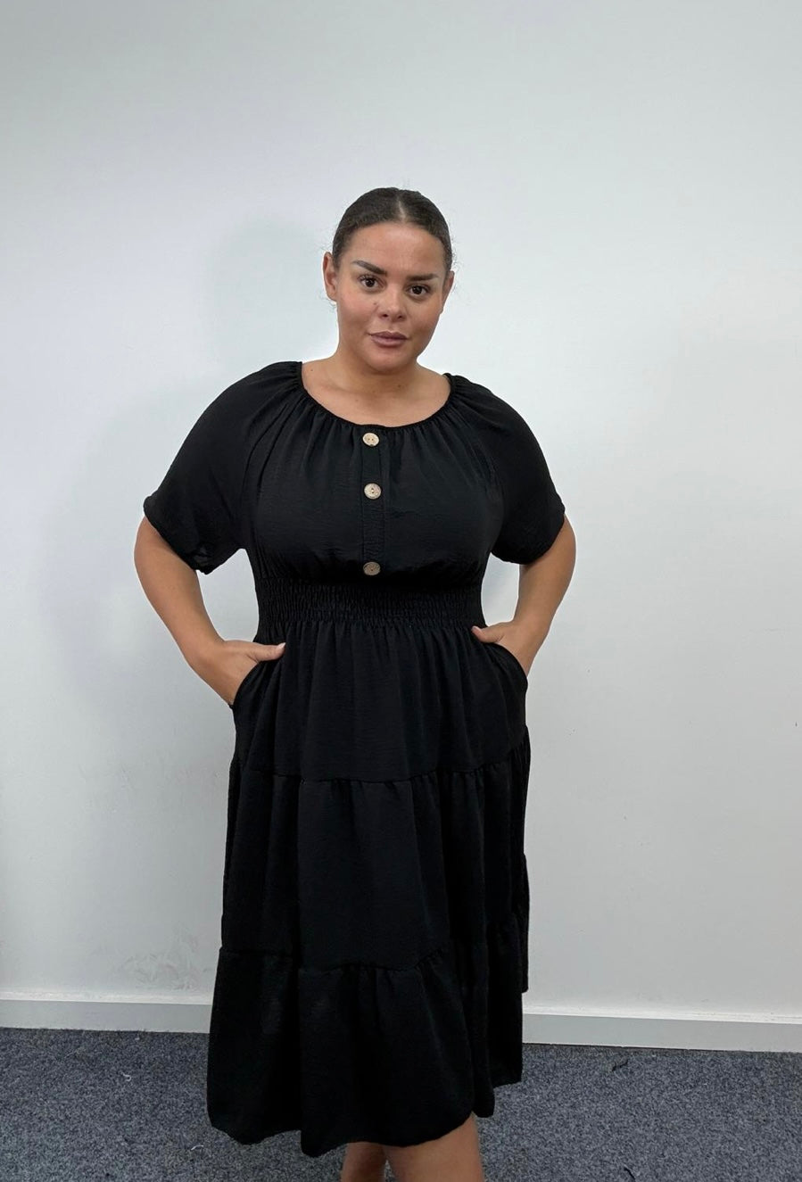 Woman wearing a Plus Size Black Button Detail Tiered Midi Dress with Pockets with buttons against a white wall