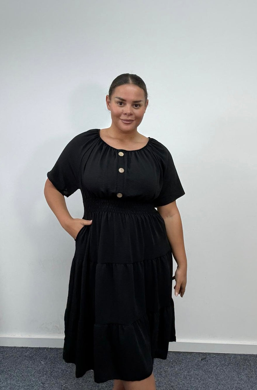 Woman wearing a Plus Size Black Button Detail Tiered Midi Dress with Pockets with buttons against a plain background