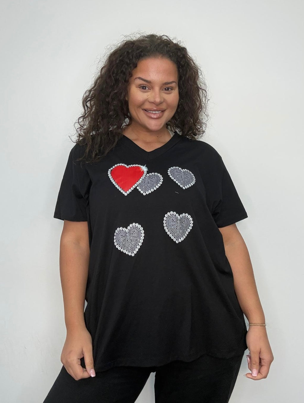 Person wearing a Plus Size Black Heart Embellished V-Neck T-Shirt with heart designs on a plain background