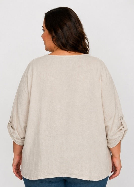 A woman shown from the back wearing a light beige linen-blend top with rolled three-quarter sleeves and blue jeans, against a plain light gray studio background.