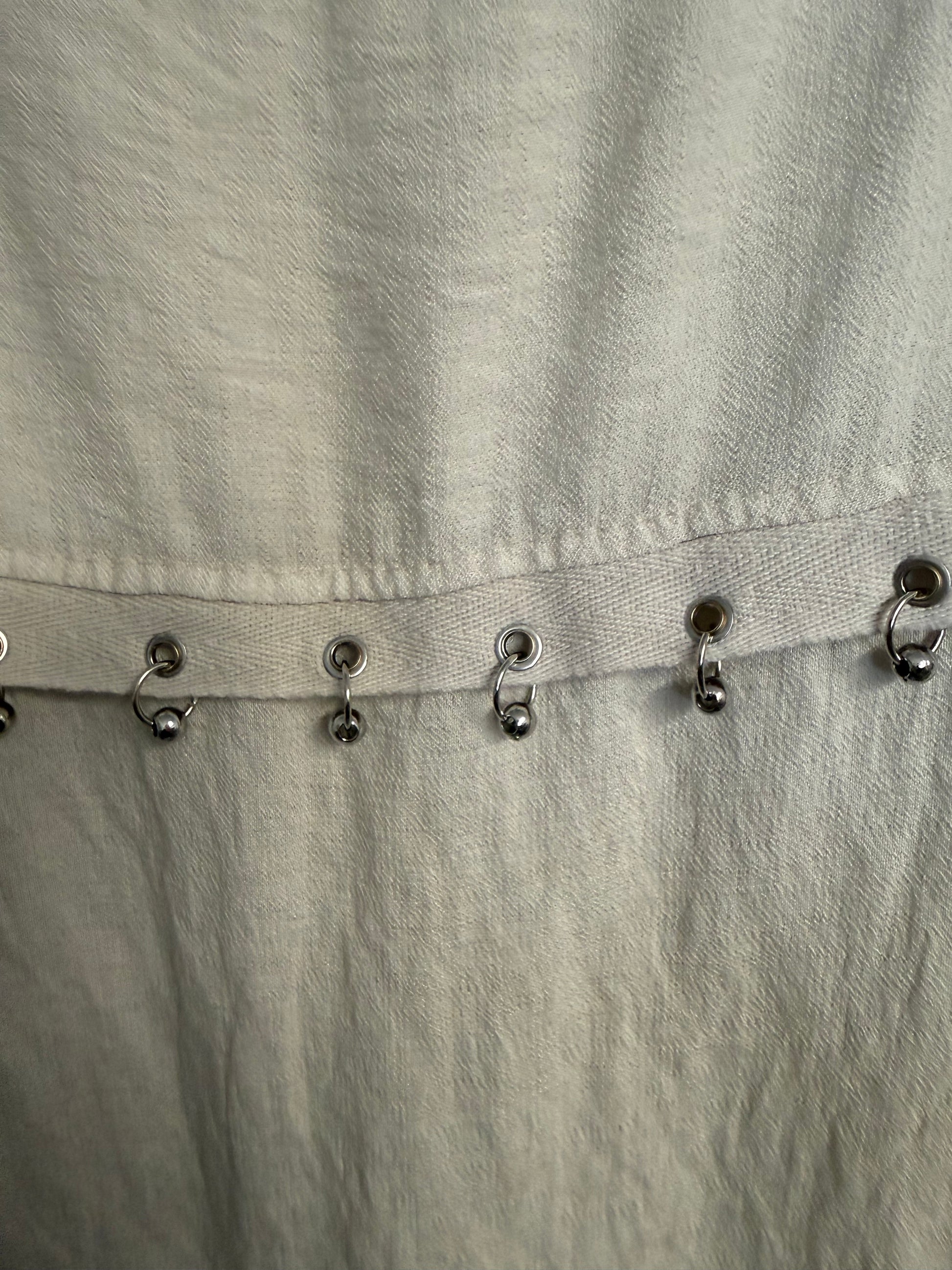 Close-up of a light beige textured fabric garment with a vertical row of metal rings with beads on.
