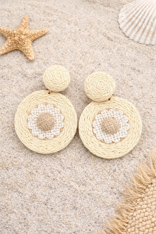 Beige raffia earrings with pearl-like centers on a sandy background with starfish and shells.