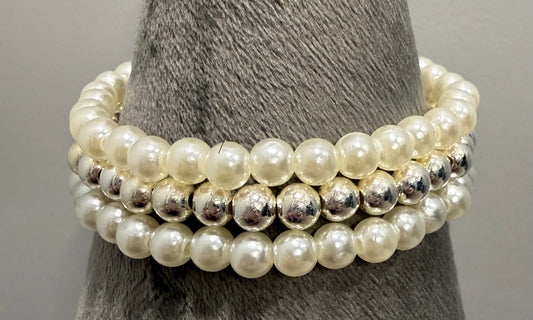 Three stacked stretch bracelets featuring cream faux-pearl beads and polished silver-tone spacer beads, displayed on a gray textured cone stand.