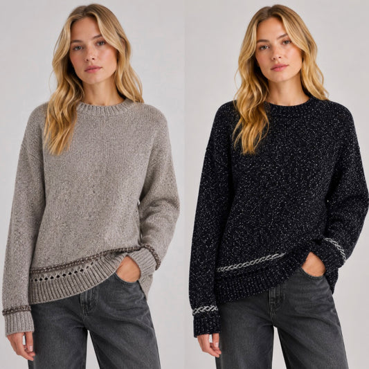 Two women modeling knit crewneck sweaters side by side against a light gray studio background. The left sweater is light taupe-gray, and the right sweater is very dark navy with subtle flecks and a contrasting light gray knit band near the hem and cuffs.