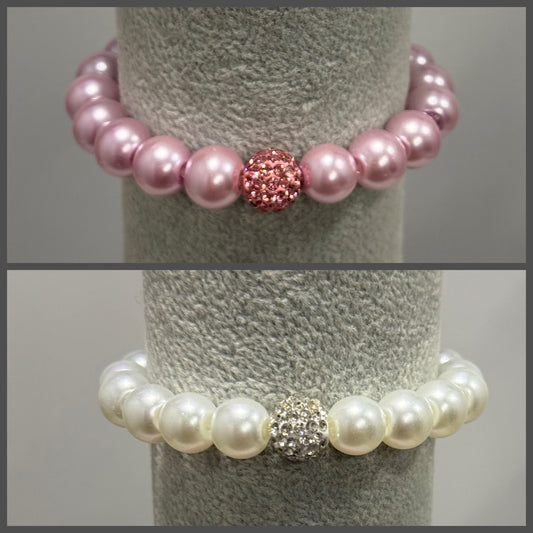 Two pearl beaded stretch bracelets displayed on a gray jewelry stand. The top bracelet features light pink pearls with a central pink rhinestone-encrusted bead.