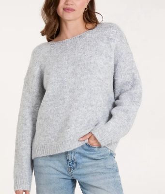 Woman wearing a light gray sweater and blue jeans on a white background