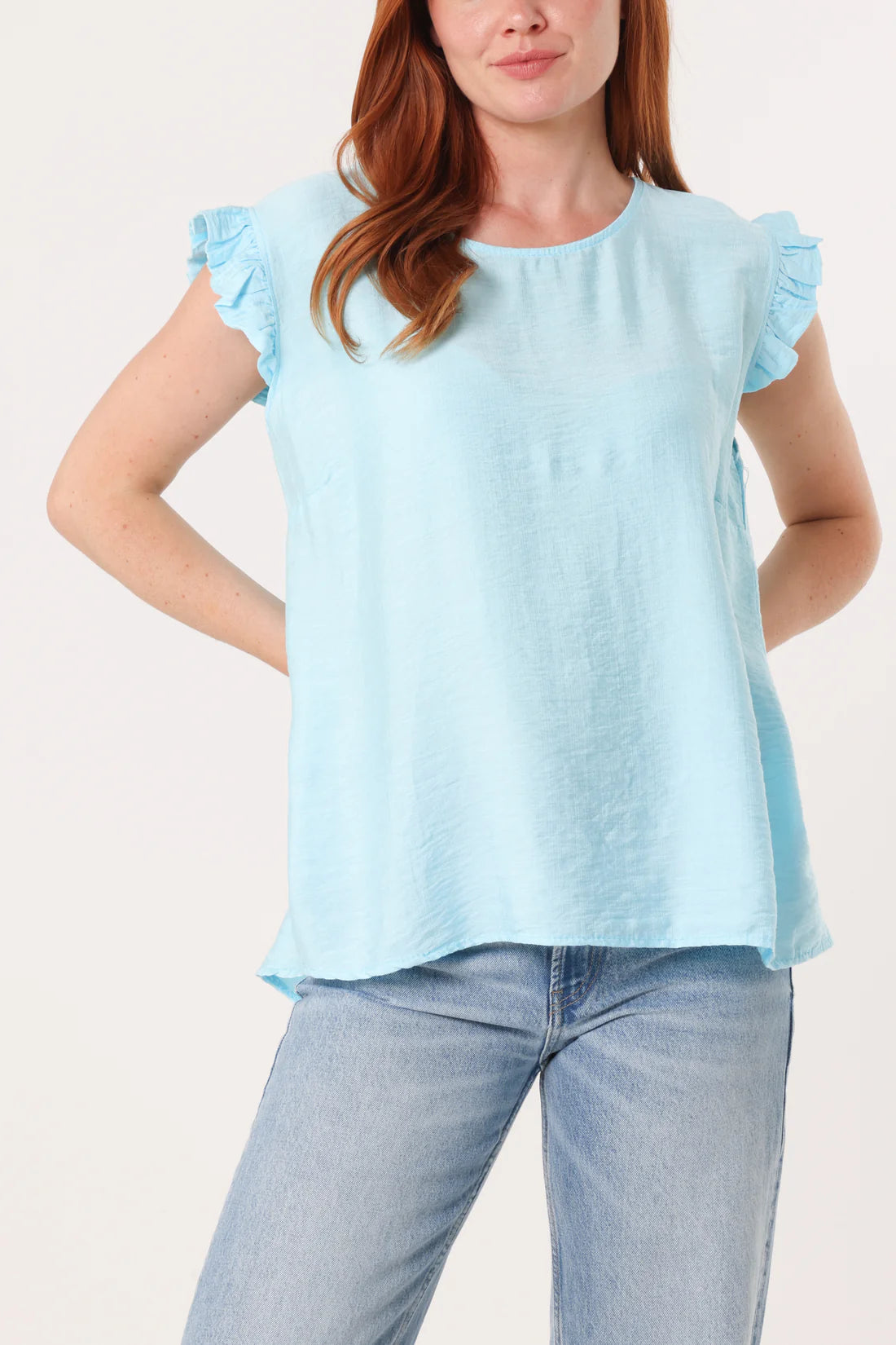Woman wearing a light blue top with ruffled sleeves and jeans on a white background