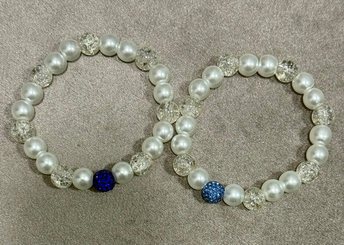 Two pearl beaded stretch bracelets with clear faceted beads and one blue rhinestone accent each, displayed on a textured gray background.