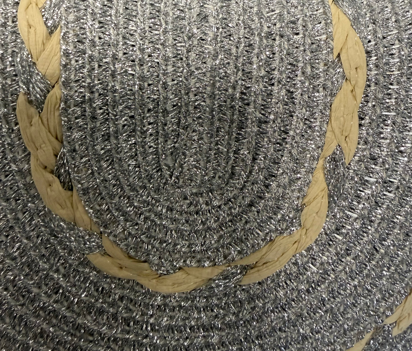 Close-up of a woven straw bag showing a textured silver colour with a decorative beige braided accent band.