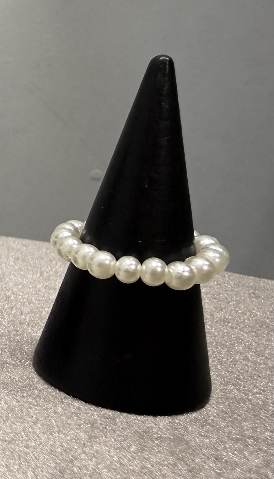 A white pearl beaded stretch bracelet displayed on a black cone jewelry stand against a gray background.