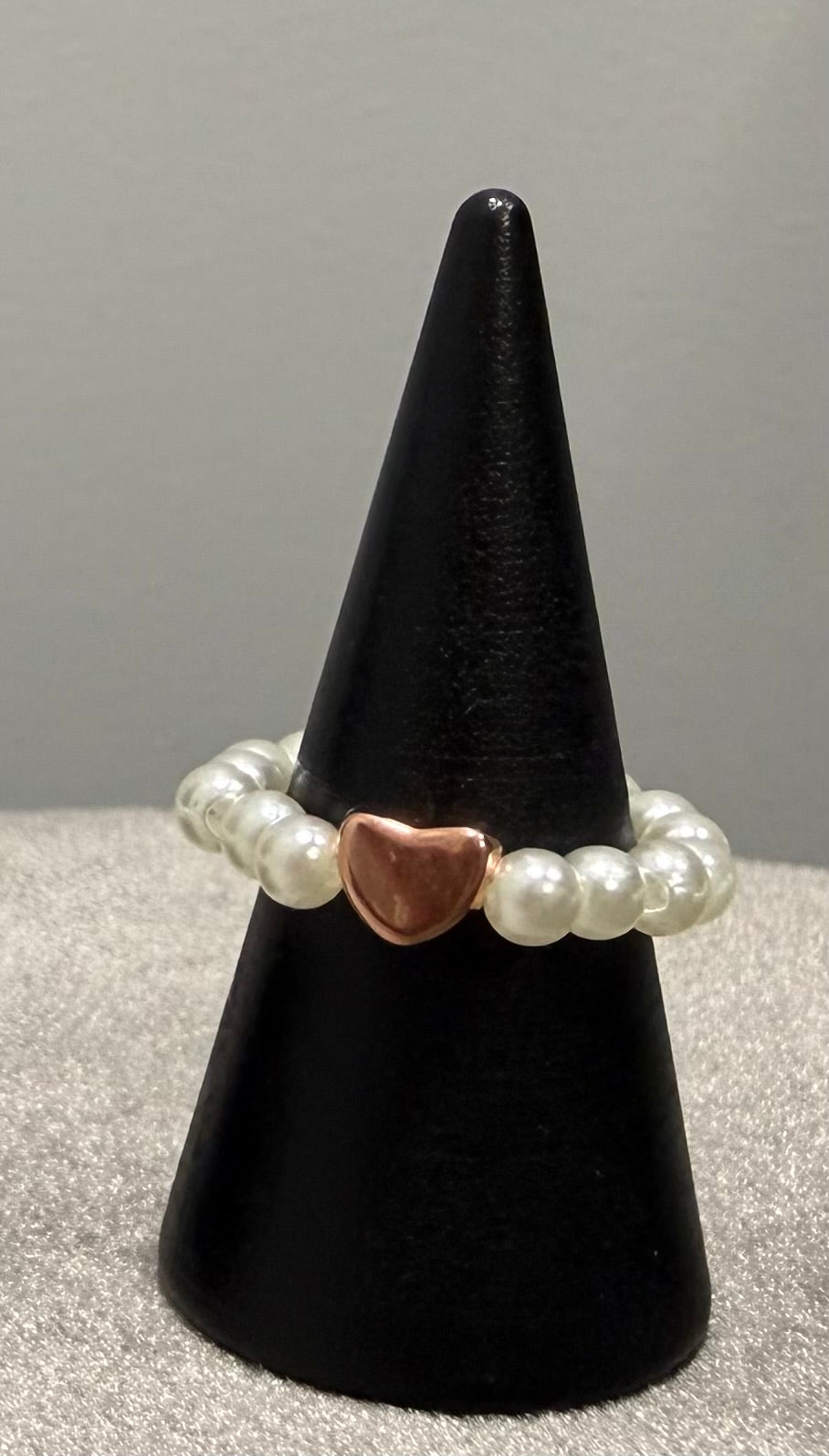 A beaded stretch bracelet with white pearl-like beads and a central rose gold heart charm, displayed on a black cone stand.