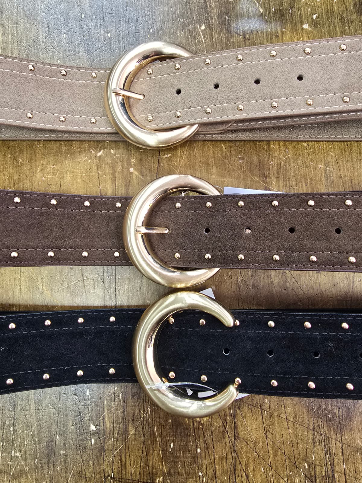 Three belts with gold buckles on a wooden surface