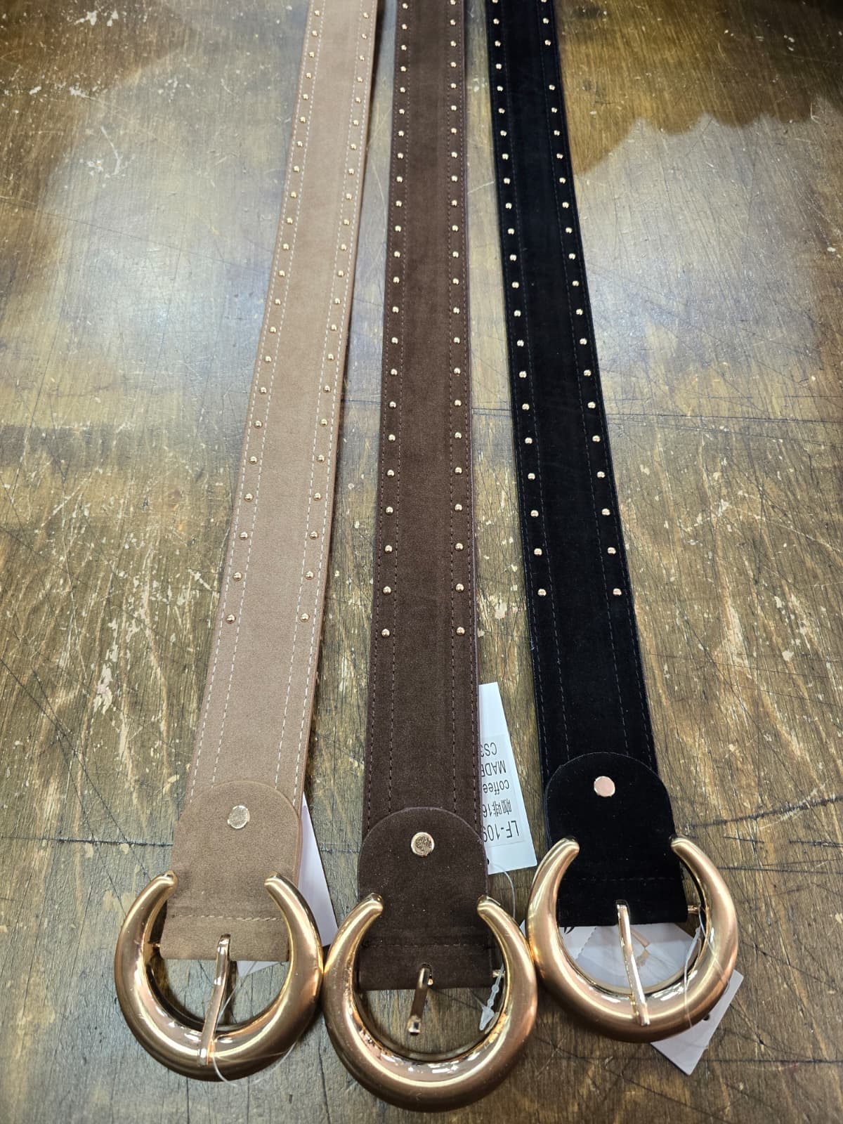 Three belts with gold buckle on a wooden surface