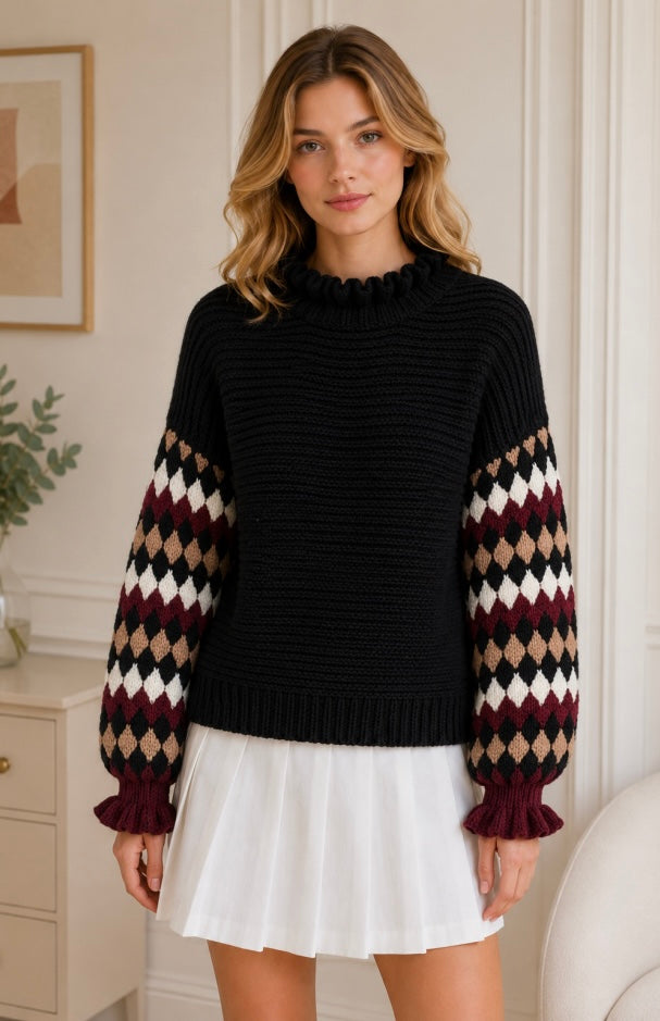 A woman wearing a black ribbed knit sweater with long sleeves featuring an argyle pattern in burgundy, beige, and white, paired with a white pleated mini skirt, standing in a brightly lit indoor room.