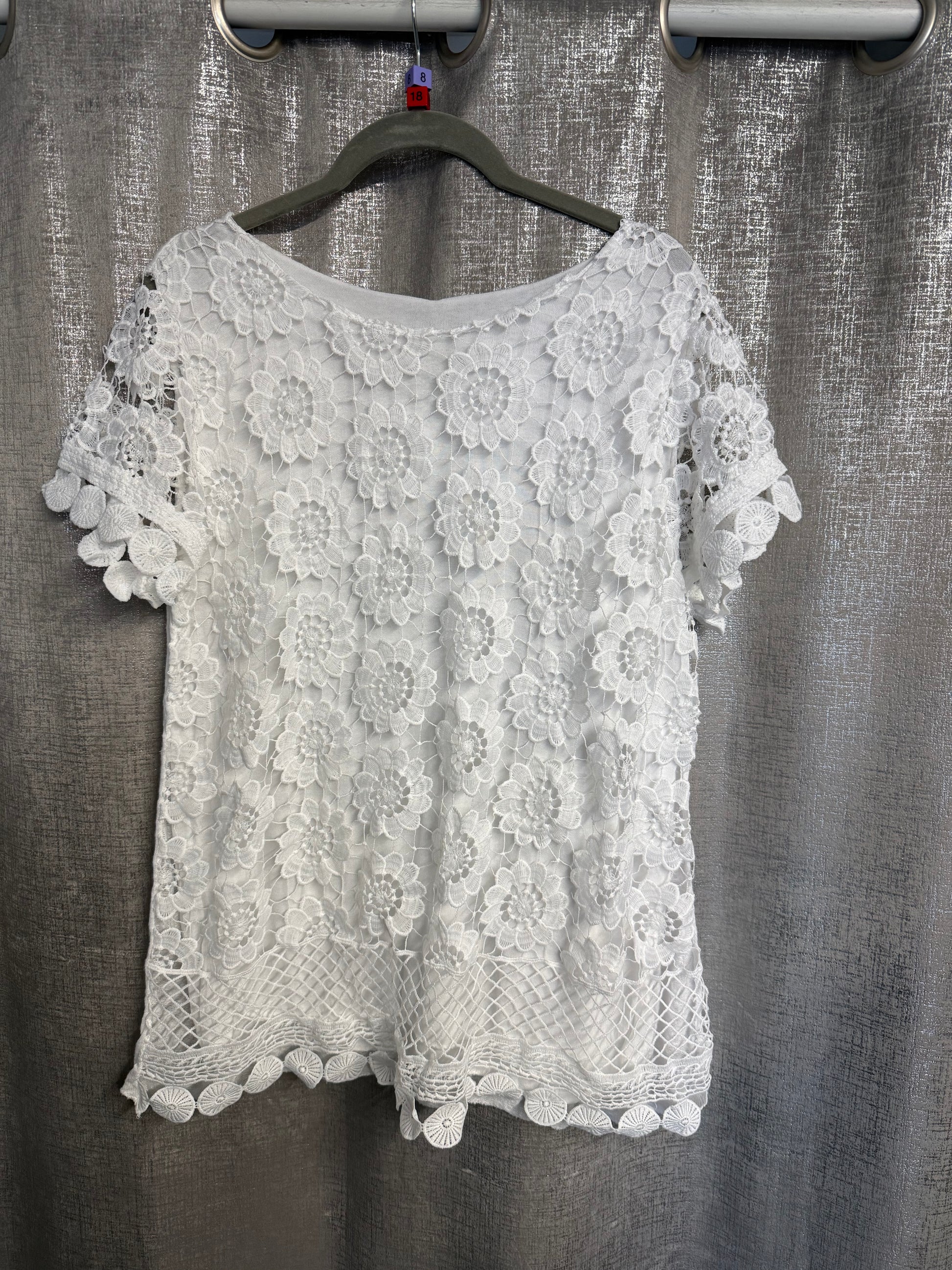 White lace top on a hanger against a textured gray background