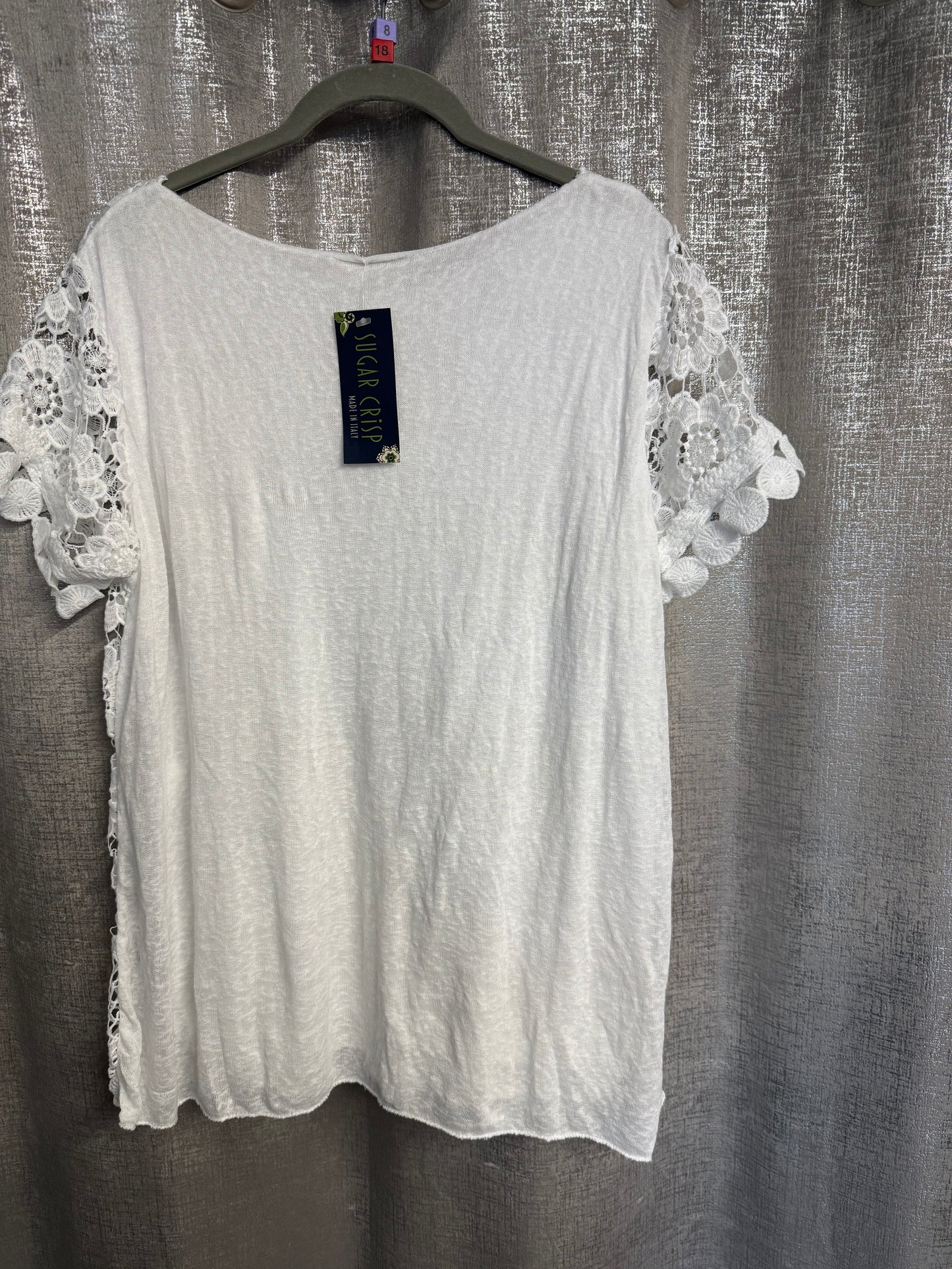 White lace-trimmed top on a hanger against a textured gray background