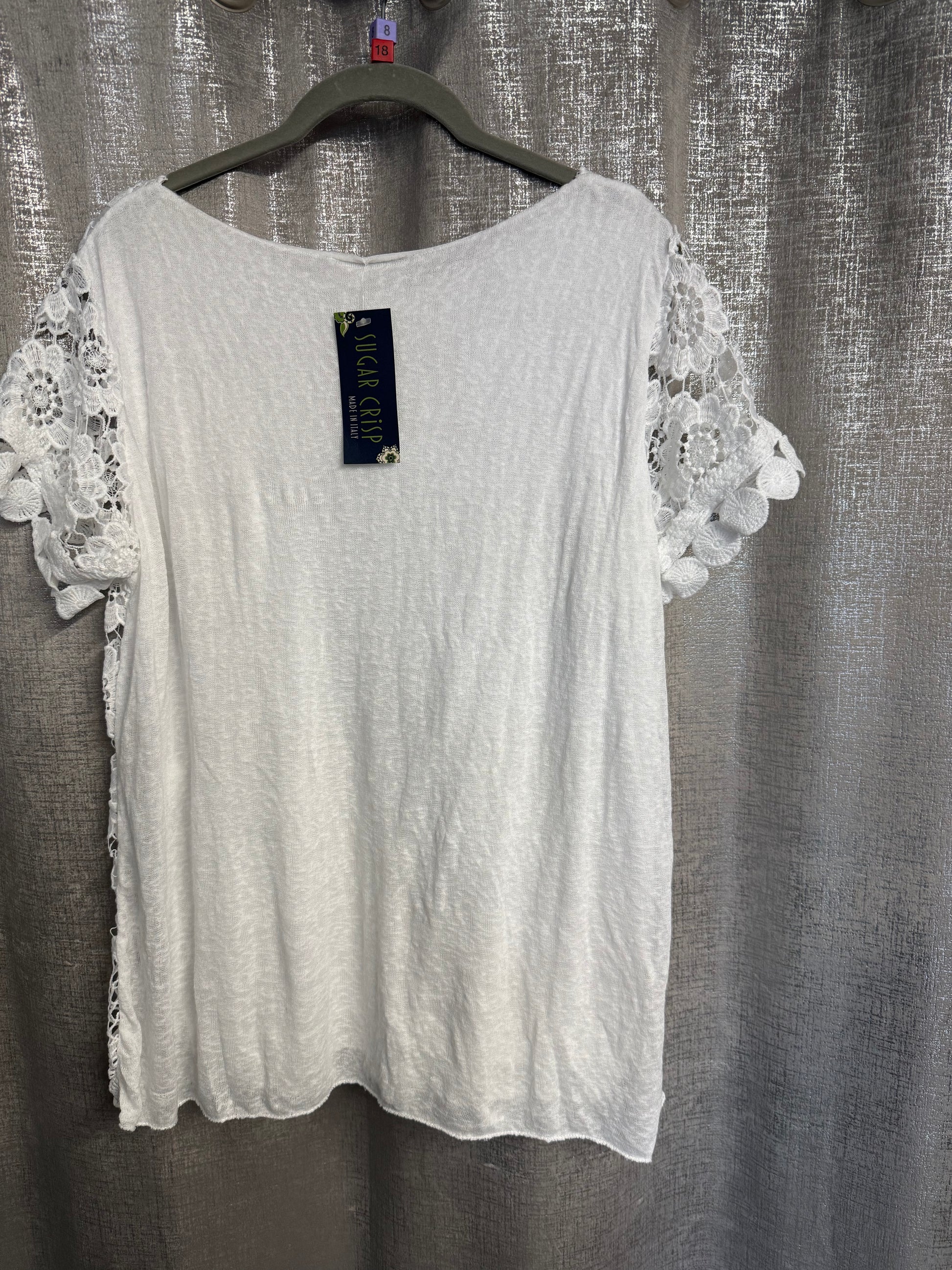 White lace-trimmed top on a hanger against a textured gray background