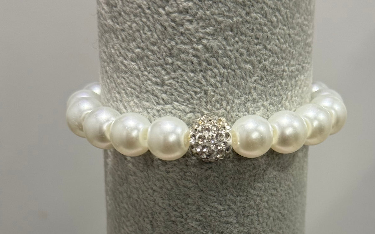 A pearl beaded bracelet with a central silver rhinestone cluster accent, displayed on a gray textured jewelry stand.