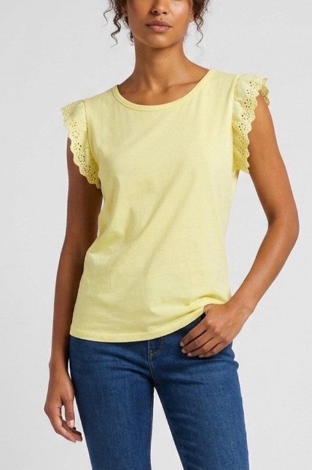 Woman wearing a yellow top with lace sleeves and blue jeans on a white background
