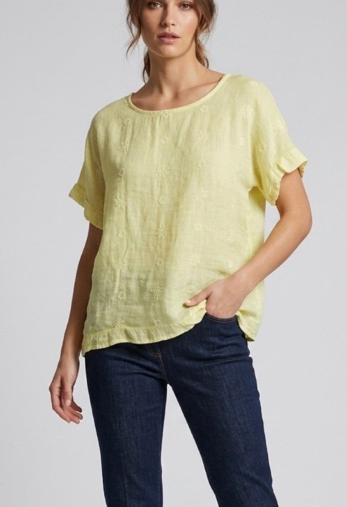 Woman wearing a light yellow top and dark blue jeans on a plain background