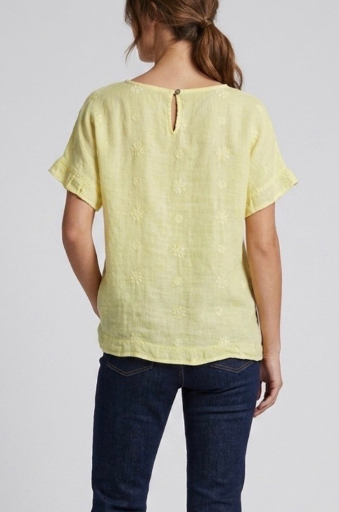 Back view of Person wearing a light yellow top and dark blue jeans on a plain background