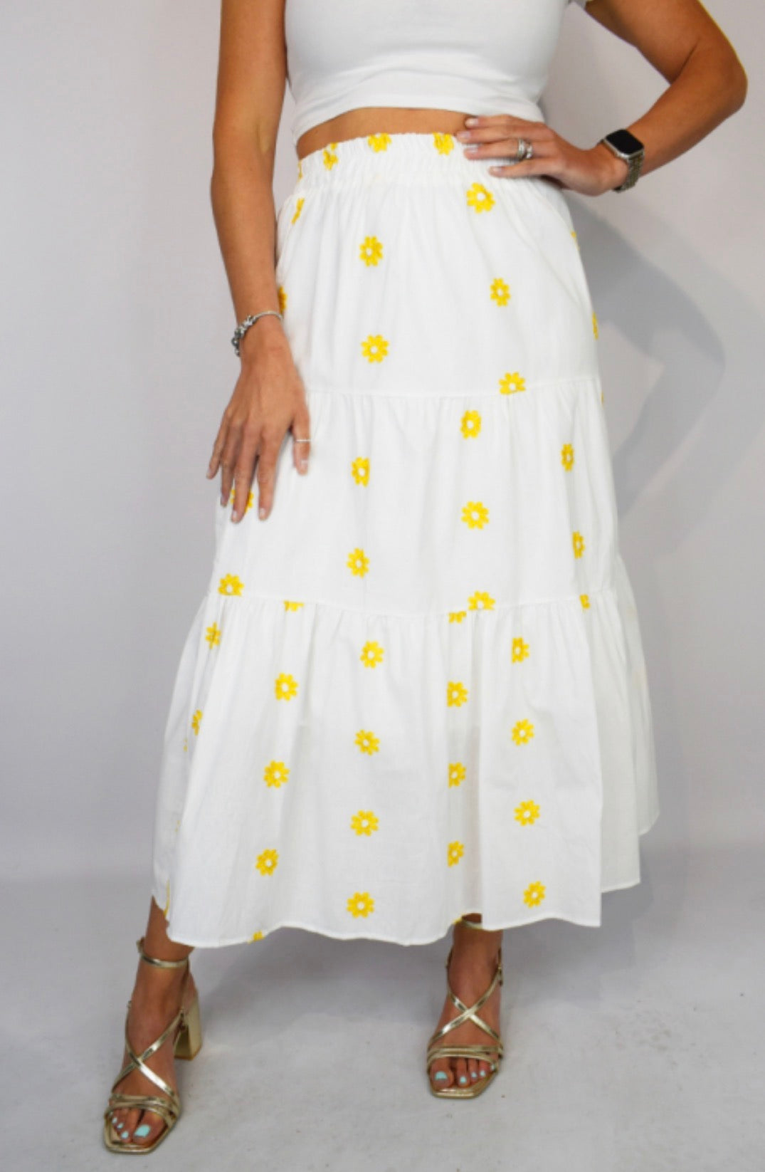 White skirt with yellow floral patterns worn by a person on a plain background