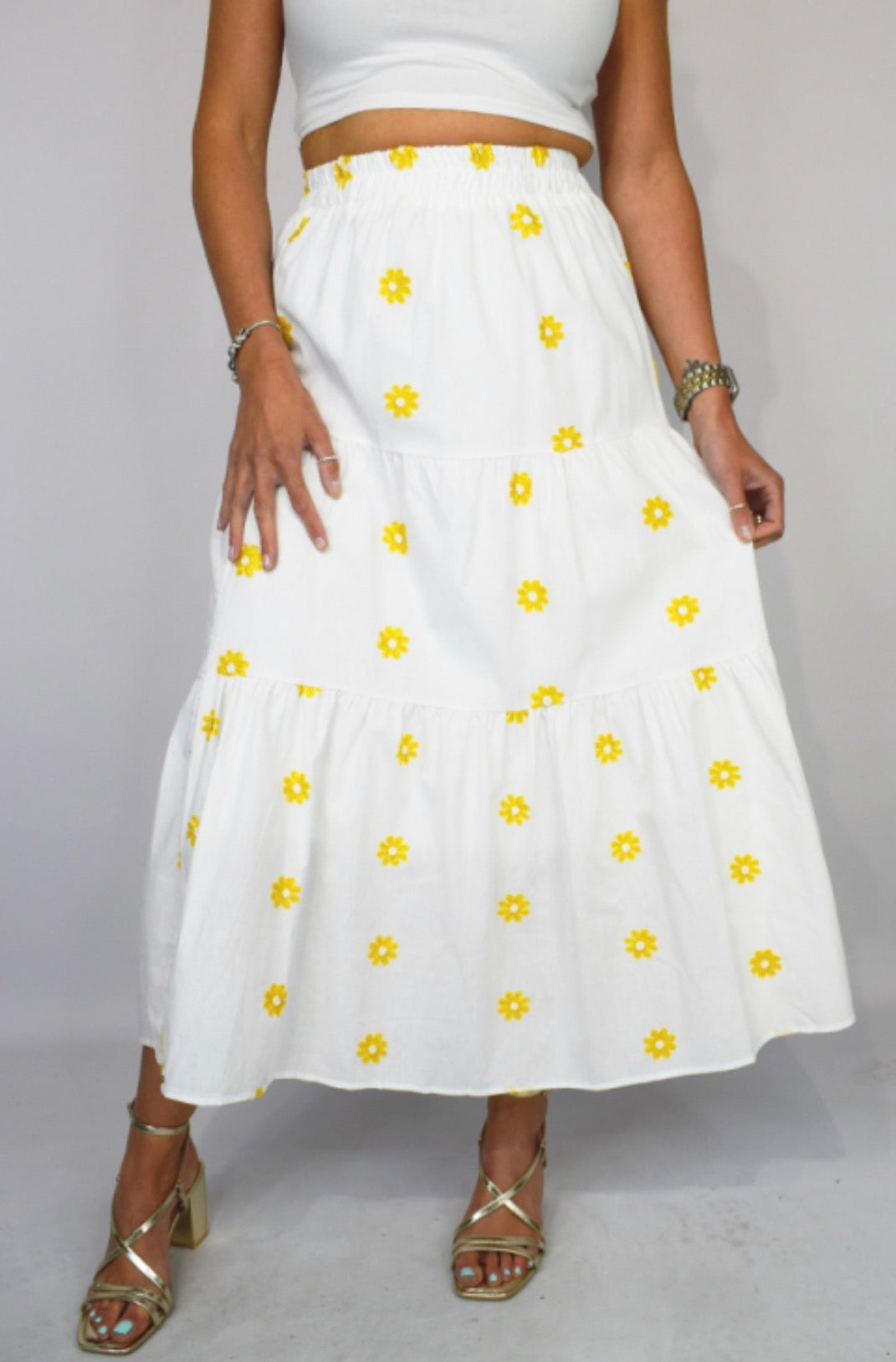 White skirt with yellow floral patterns worn by a person on a plain background